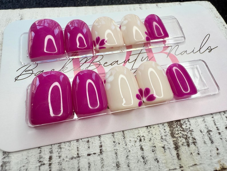 May include: Two sets of press-on nails. Each set has a mix of solid magenta and off-white nails. The off-white nails have a magenta floral design. The nails are displayed on a white card with the text "Back Beauty Nails".