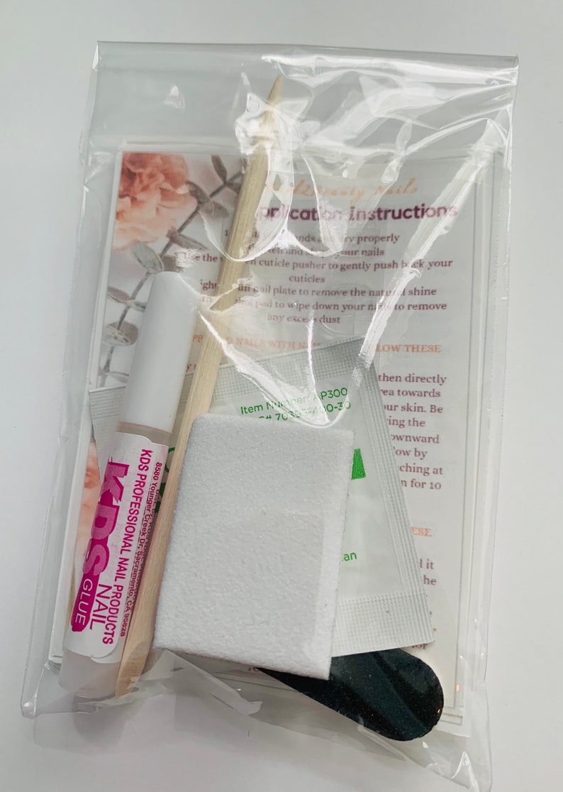 Puede incluir: Una bolsa de pl&aacute;stico transparente que contiene un juego de suministros para el arte de u&ntilde;as. El juego incluye una peque&ntilde;a botella de pegamento para u&ntilde;as etiquetada como "KDS Professional Nail Products", un empujador de cut&iacute;culas de madera, una lima de u&ntilde;as blanca, un peque&ntilde;o paquete blanco y una lima de u&ntilde;as negra. La bolsa tambi&eacute;n incluye una peque&ntilde;a tarjeta con instrucciones para aplicar el arte de u&ntilde;as.