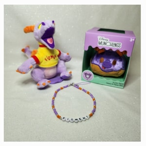 May include: A purple plush dragon toy with orange accents and a yellow shirt that says "Figment". A matching beaded necklace spells out "Figment". A "Disney Munchlings" box contains a plush donut.