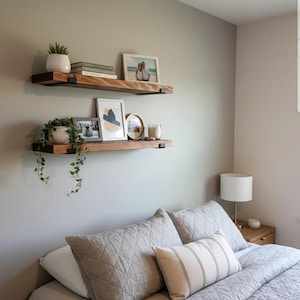 Peut inclure: Deux &eacute;tag&egrave;res flottantes en bois avec des supports en m&eacute;tal noir sont fix&eacute;es &agrave; un mur gris clair. L'&eacute;tag&egrave;re sup&eacute;rieure contient une plante en pot, des livres et une photo encadr&eacute;e. L'&eacute;tag&egrave;re inf&eacute;rieure pr&eacute;sente une plante, des photos encadr&eacute;es et une bougie. Les &eacute;tag&egrave;res sont au-dessus d'un lit avec une literie grise.