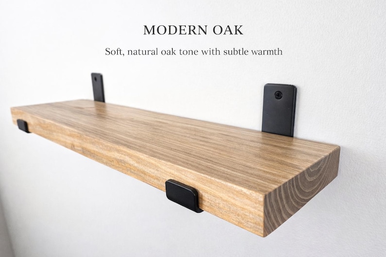 Peut inclure: &Eacute;tag&egrave;re flottante en ch&ecirc;ne clair avec des supports en m&eacute;tal noir, fix&eacute;e &agrave; un mur blanc. Le texte indique &laquo; MODERN OAK &raquo; et &laquo; Soft, natural oak tone with subtle warmth &raquo;. Design moderne.