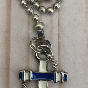 以下が含まれることがあります： 青と白のアンカーチャームが付いたシルバーチェーン。アンカーはロープのデザインで囲まれています。