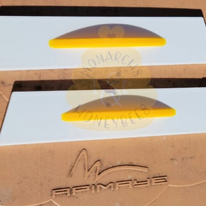 May include: Two white plastic beehive frames with yellow plastic inserts. The frames are labeled "Monarch's Honeybees".