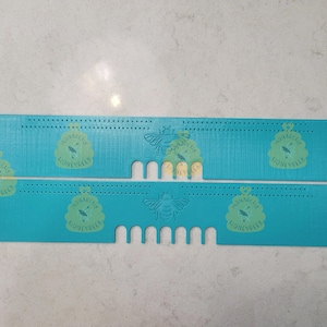 May include: Two turquoise blue plastic weaving looms with a bee and honeycomb logo. The looms have rows of holes for weaving.