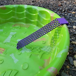 May include: A green plastic kiddie pool with a purple handle. The pool has a white fish design and the words "Little Tikes" printed on the side.
