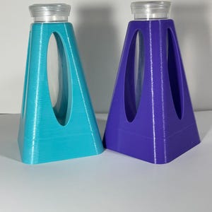 Puede incluir: Dos soportes en forma de pir&aacute;mide impresos en 3D, en color turquesa y morado, cada uno con un cilindro de vidrio transparente en el centro.
