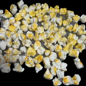 Puede incluir: Un montón de palomitas de maíz blancas con granos amarillos. Las palomitas de maíz están esparcidas sobre una superficie blanca.