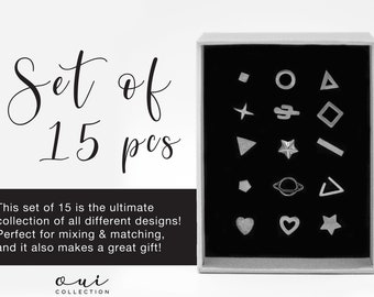 Puede incluir: Un conjunto de 15 pendientes de botón plateados en diversas formas geométricas y de fantasía, incluyendo estrellas, corazones y triángulos, presentados en una caja blanca con interior negro. El texto "Set of 15 pcs" está encima de la caja.