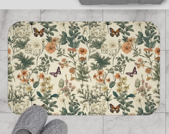 Könnte beinhalten: Eine cremefarbene Badematte mit einem Blumen- und Schmetterlingsmuster. Das Muster zeigt verschiedene Blumen, Blätter und Schmetterlinge in Orange-, Rosa-, Grün- und Brauntönen.