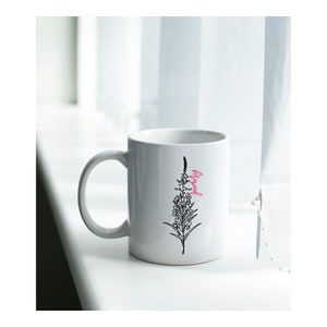 May include: White ceramic mug with a black line drawing of a flower and the word "Blessed" in pink lettering.