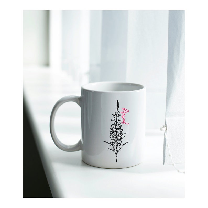 May include: White ceramic mug with a black line drawing of a flower and the word "Blessed" in pink lettering.