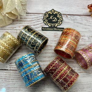 May include: Six sets of colorful bangles with gold accents. The bangles are stacked and wrapped in plastic. The bangles are in the colors gold, black, orange, purple, blue, and red.