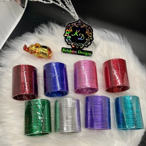 May include: A set of eight colorful metal bangles, each with a shiny metallic finish. The bangles are stacked in a pile, with the colors red, blue, pink, green, silver, purple, and teal visible. The bangles are packaged in clear plastic wrap.