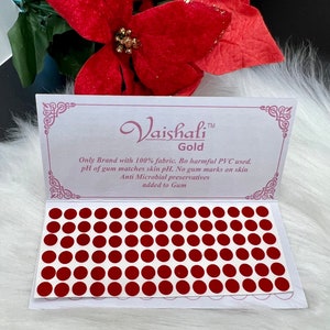May include: A sheet of 72 red round adhesive bindi stickers. The sheet is white with a border and the text "Vaishali™ Gold Only Brand with 100% fabric. Bo harmful PVC used. pH of gum matches skin pH. No gum marks on skin Anti Microbial preservatives added to Gum".