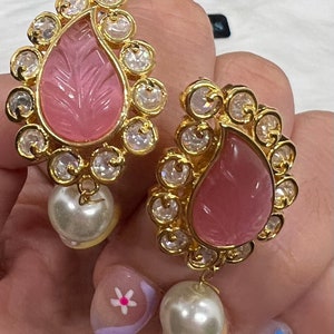 Pode incluir: Um par de brincos de ouro com detalhes em pedra rosa e gotas de pérola. Os brincos têm um design em forma de lágrima com um padrão floral.
