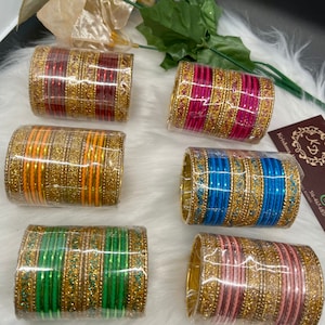 May include: Six sets of gold bangles with different colored glass. Each set has a gold design and glitter.