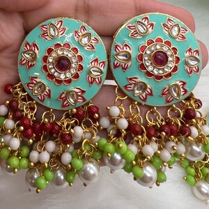 May include: A pair of turquoise blue earrings with intricate floral designs and red accents. The earrings have a dangling chain with white, green, and red beads.