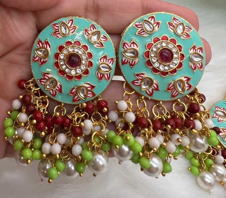 May include: A pair of turquoise blue earrings with intricate floral designs and red accents. The earrings have a dangling chain with white, green, and red beads.