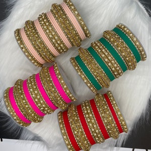 Op de afbeelding: Set van zes kleurrijke armbanden met gouden en witte versieringen. De armbanden zijn gemaakt van een stoffen materiaal en hebben een gelaagd ontwerp.