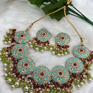 May include: A turquoise and gold necklace set with red and white floral designs. The necklace has multiple layers of pearls and beads in white, green, and maroon.