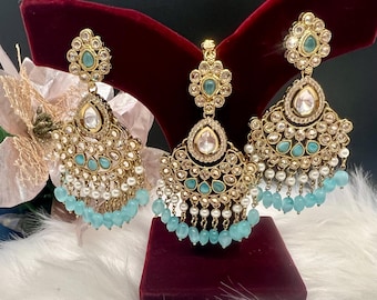 Puede incluir: Un par de pendientes de tono dorado con piedras turquesa y blancas, y un collar colgante a juego. Los pendientes y el collar presentan un diseño en forma de lágrima con flecos de cuentas.