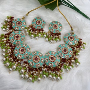 May include: A turquoise and gold necklace with red and white enamel detailing. The necklace features multiple round pendants with intricate floral designs and is adorned with white and green pearl beads.