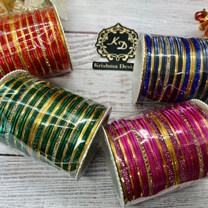 Op de afbeelding: Vier sets armbanden in rood, groen, blauw en paars met gouden accenten. Elke set is verpakt in een doorzichtige plastic container.