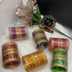 May include: Six sets of colorful bangles with gold accents. The bangles are stacked and wrapped in clear plastic. The bangles are purple, black, red, orange, and green.