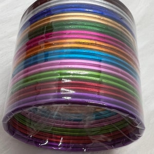 May include: A stack of colorful bangles in a variety of metallic shades, including silver, gold, purple, green, blue, and pink. The bangles are arranged in a circular pattern and are wrapped in clear plastic.