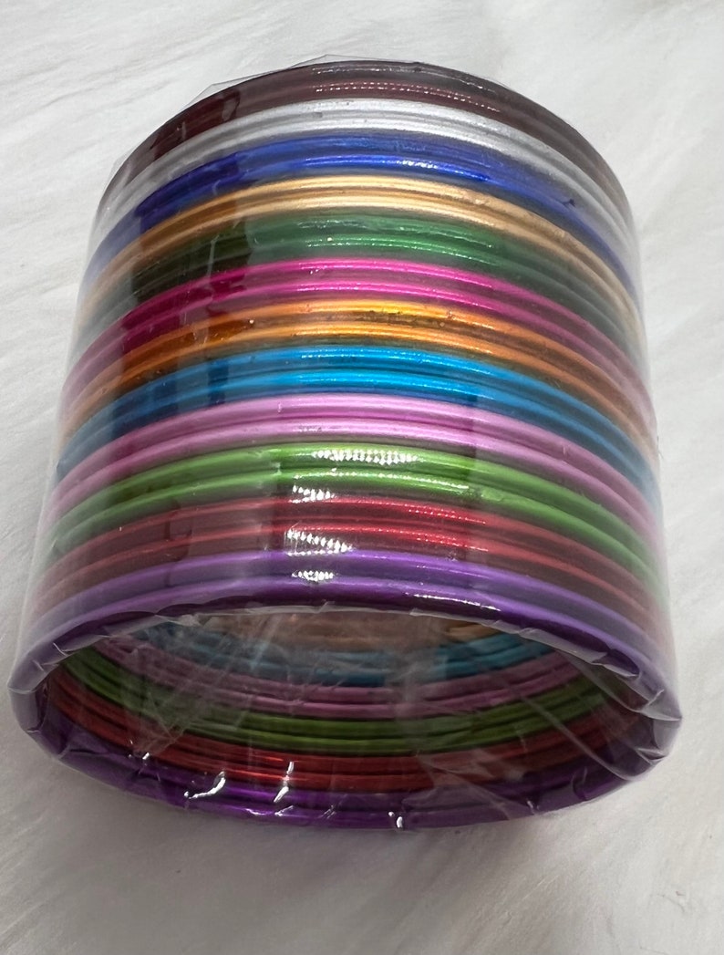 May include: A stack of colorful bangles in a variety of metallic shades, including silver, gold, purple, green, blue, and pink. The bangles are arranged in a circular pattern and are wrapped in clear plastic.