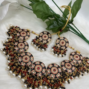 May include: A black and red necklace with round pendants and pearl and red bead accents. The necklace is made of metal and has a gold finish.