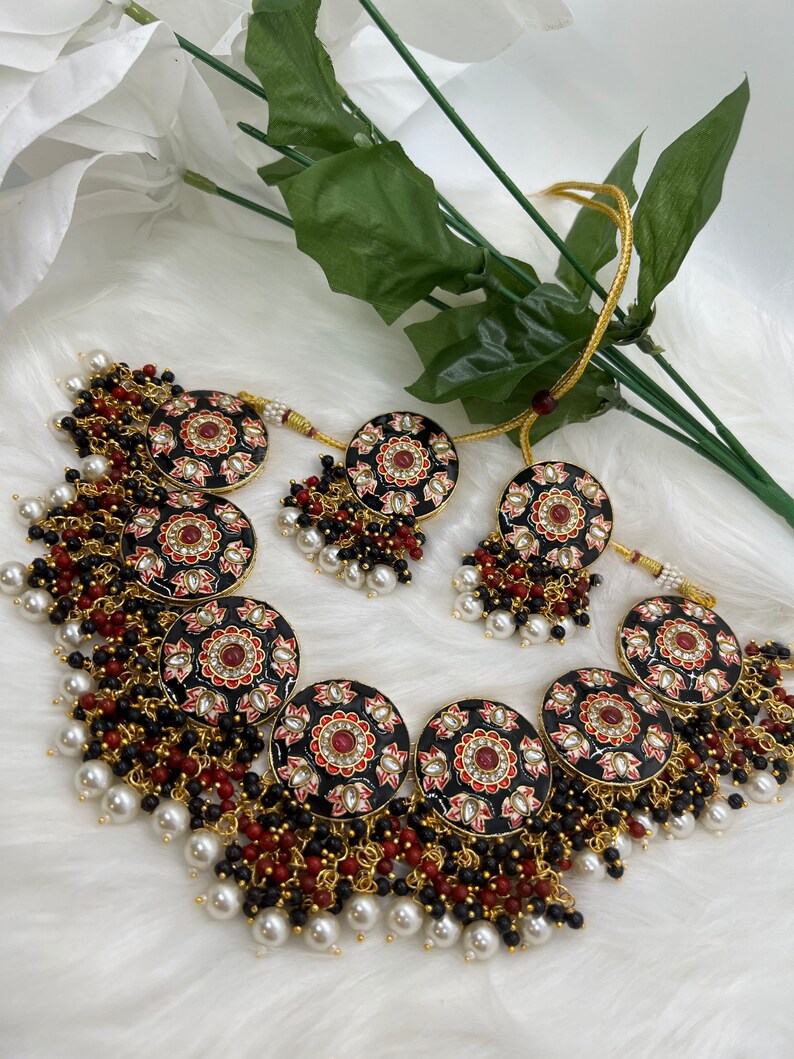 May include: A black and red necklace with round pendants and pearl and red bead accents. The necklace is made of metal and has a gold finish.