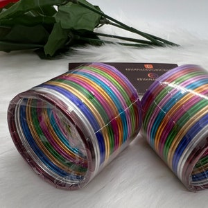 May include: Two sets of colorful metal bangles packaged in clear plastic. The bangles are arranged in a stack and are a variety of colors, including silver, gold, pink, purple, blue, green, and red.