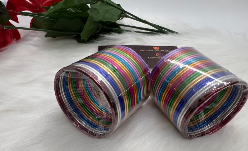 May include: Two sets of colorful metal bangles packaged in clear plastic. The bangles are arranged in a stack and are a variety of colors, including silver, gold, pink, purple, blue, green, and red.
