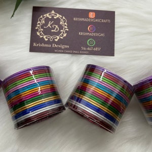 May include: Set of four colorful metal bangles, each with multiple layers of different colored metal bands. The bangles are stacked together and have a purple base.