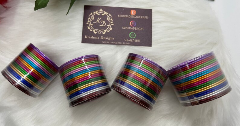 May include: Set of four colorful metal bangles, each with multiple layers of different colored metal bands. The bangles are stacked together and have a purple base.