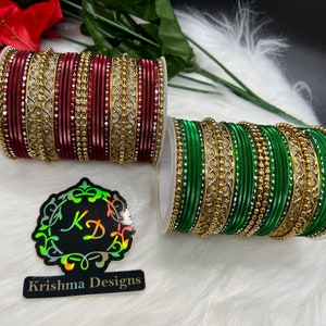 May include: Two sets of bangles, one red and one green, with gold accents and rhinestones. The bangles are stacked on top of each other and are displayed on a white fuzzy surface. The image also includes a logo for Krishna Designs.