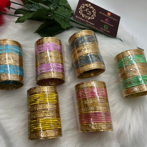 May include: Six sets of gold bangles with glitter. Each set is a different color: blue, pink, gray, green, yellow, and pink. The bangles are stacked on top of each other and are wrapped in plastic.