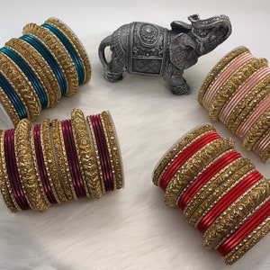 May include: Set of four bangle bracelets with gold and jeweled accents. The bracelets are in teal, burgundy, pink, and red.