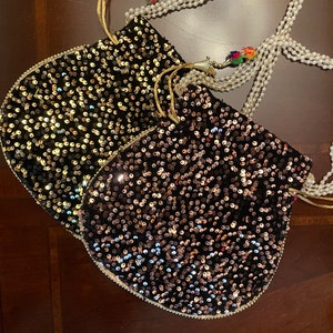 May include: Two black velvet drawstring bags with gold and silver sequins. The bags are decorated with a pearl and beaded chain.