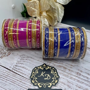 May include: Two sets of bangles, one set is pink and the other is blue. Both sets have gold accents and clear beads. The bangles are stacked and packaged in plastic.