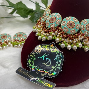 May include: A turquoise and gold necklace with red and white beads. The necklace has a circular design with floral patterns and red stones. The necklace is paired with matching earrings.