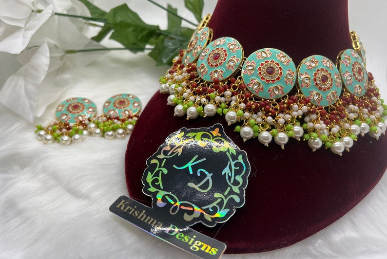 May include: A turquoise and gold necklace with red and white beads. The necklace has a circular design with floral patterns and red stones. The necklace is paired with matching earrings.