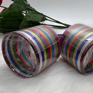 May include: A set of colorful metal bangles in a plastic package. The bangles are arranged in a circle and are all different colors, including red, orange, yellow, green, blue, purple, and silver. The bangles are shiny and have a metallic finish.