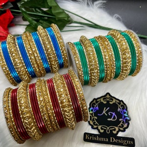 Op de afbeelding: Drie sets gouden armbanden met juweelaccenten. De armbanden zijn in rood, blauw en groen. De sets zijn gerangschikt op een wit, pluche oppervlak. De afbeelding bevat de tekst "Krishna Designs".