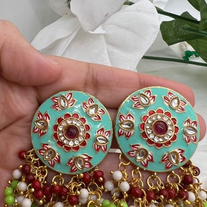 May include: A pair of turquoise blue earrings with intricate floral designs and red and white accents. The earrings have a dangling chain with white, green, and red beads.