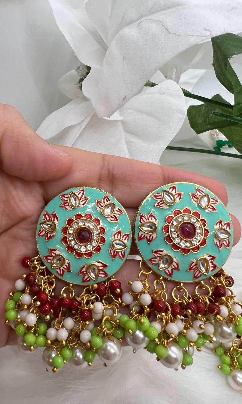 May include: A pair of turquoise blue earrings with intricate floral designs and red and white accents. The earrings have a dangling chain with white, green, and red beads.