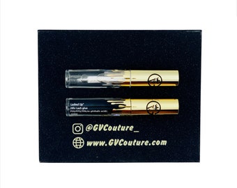 May include: Two clear tubes with gold caps containing lash glue. The tubes are on a black background with the text "Lashed Up" 24hr Lash glue, PEG/PPG/TPA/m-phthalic acid/ water, @GVCouture_ and www.GVCouture.com printed in gold.