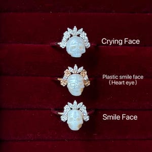 May include: Three rings with skull designs. Each ring features a white skull with different facial expressions. The skulls are adorned with floral and gem accents. The image text reads "Crying Face", "Plastic smile face (Heart eye)", and "Smile Face".