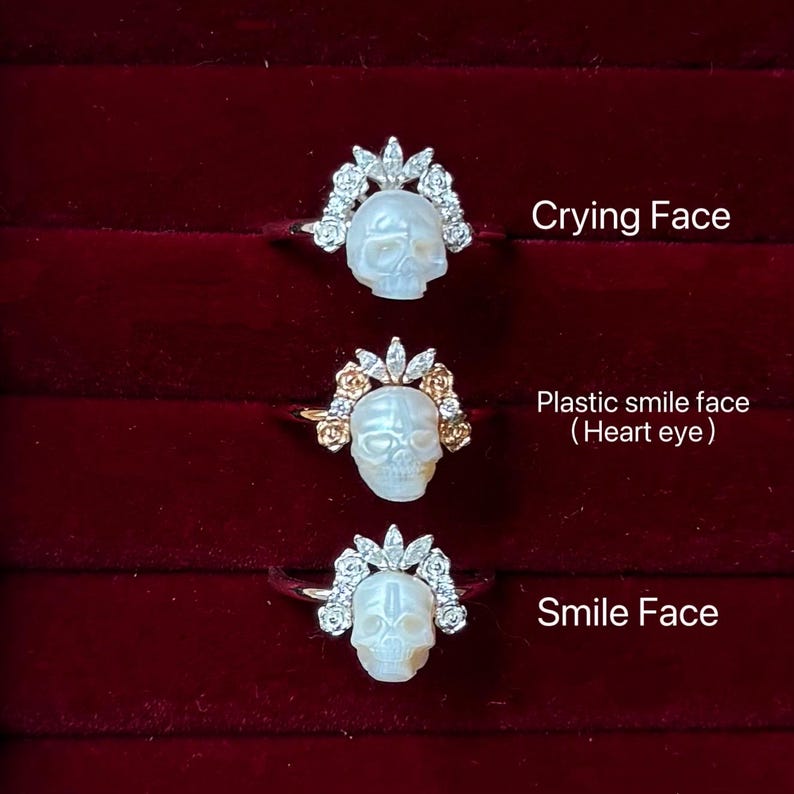 May include: Three rings with skull designs. Each ring features a white skull with different facial expressions. The skulls are adorned with floral and gem accents. The image text reads "Crying Face", "Plastic smile face (Heart eye)", and "Smile Face".